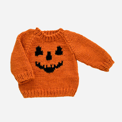 An orange knit baby sweater featuring a black knitted jack-o'-lantern face on the front, displayed against a light gray background.