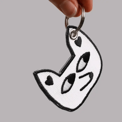 Keychain with black and white design held by a hand against a gray background