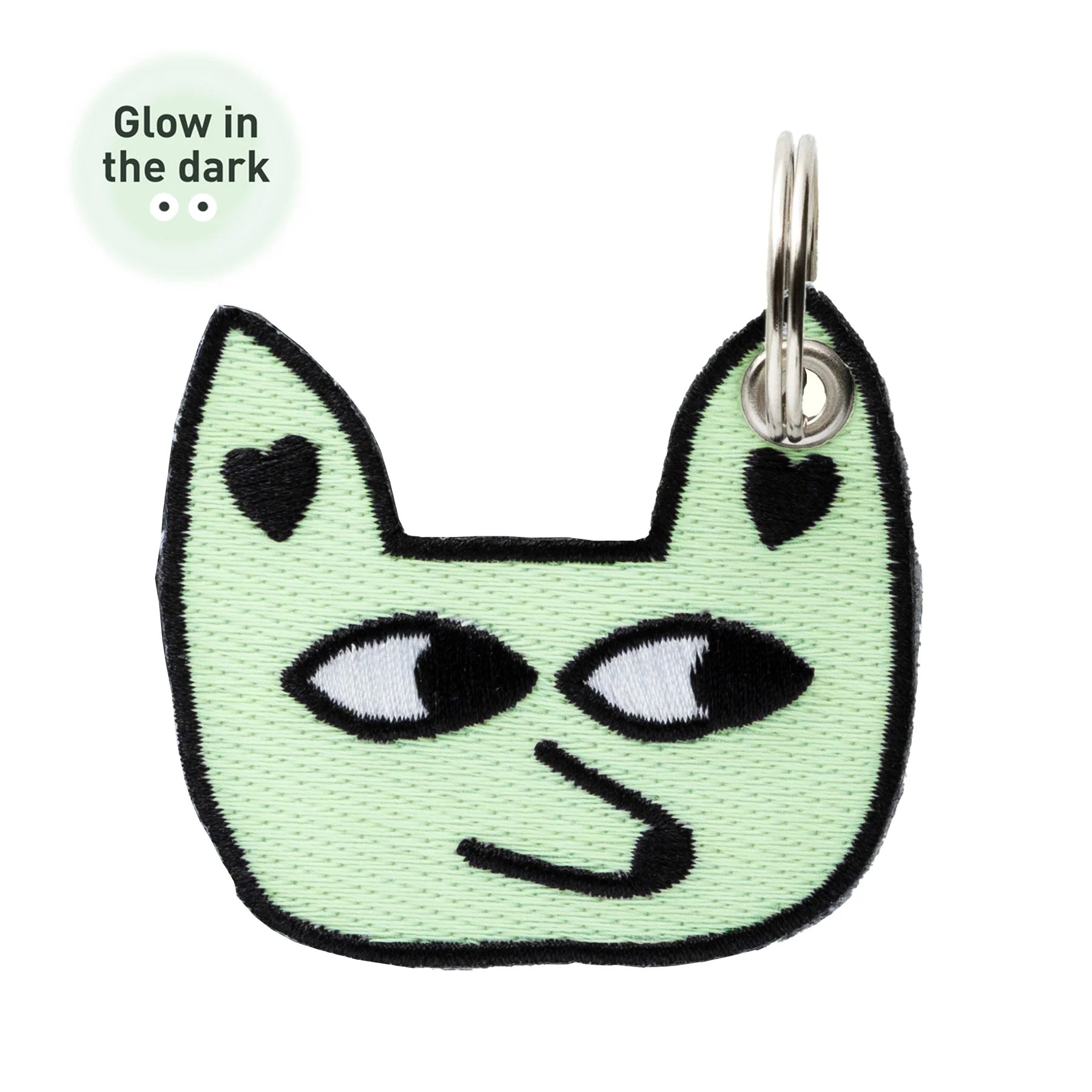A mint green embroidered patch shaped like a cat head with black outlines, white eyes, and small black heart details on the ears, shown on a white background with a small 'Glow in the dark' callout.