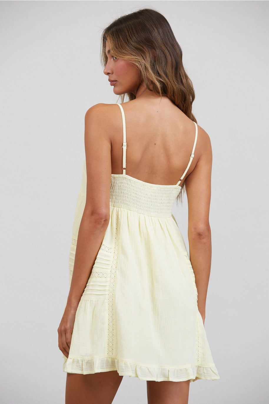 Woman wearing a light yellow dress with thin straps on a plain background