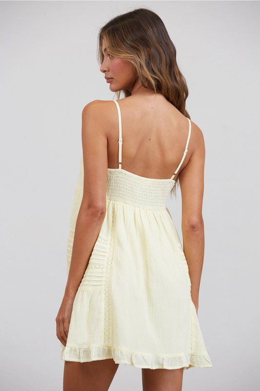 Woman wearing a light yellow dress with thin straps on a plain background
