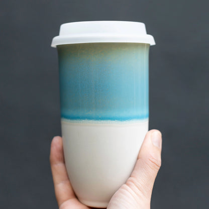 Hand holding blue and white ceramic travel mug on grey background. Nova ceramics. sustainable coffee and tea travel mug. 