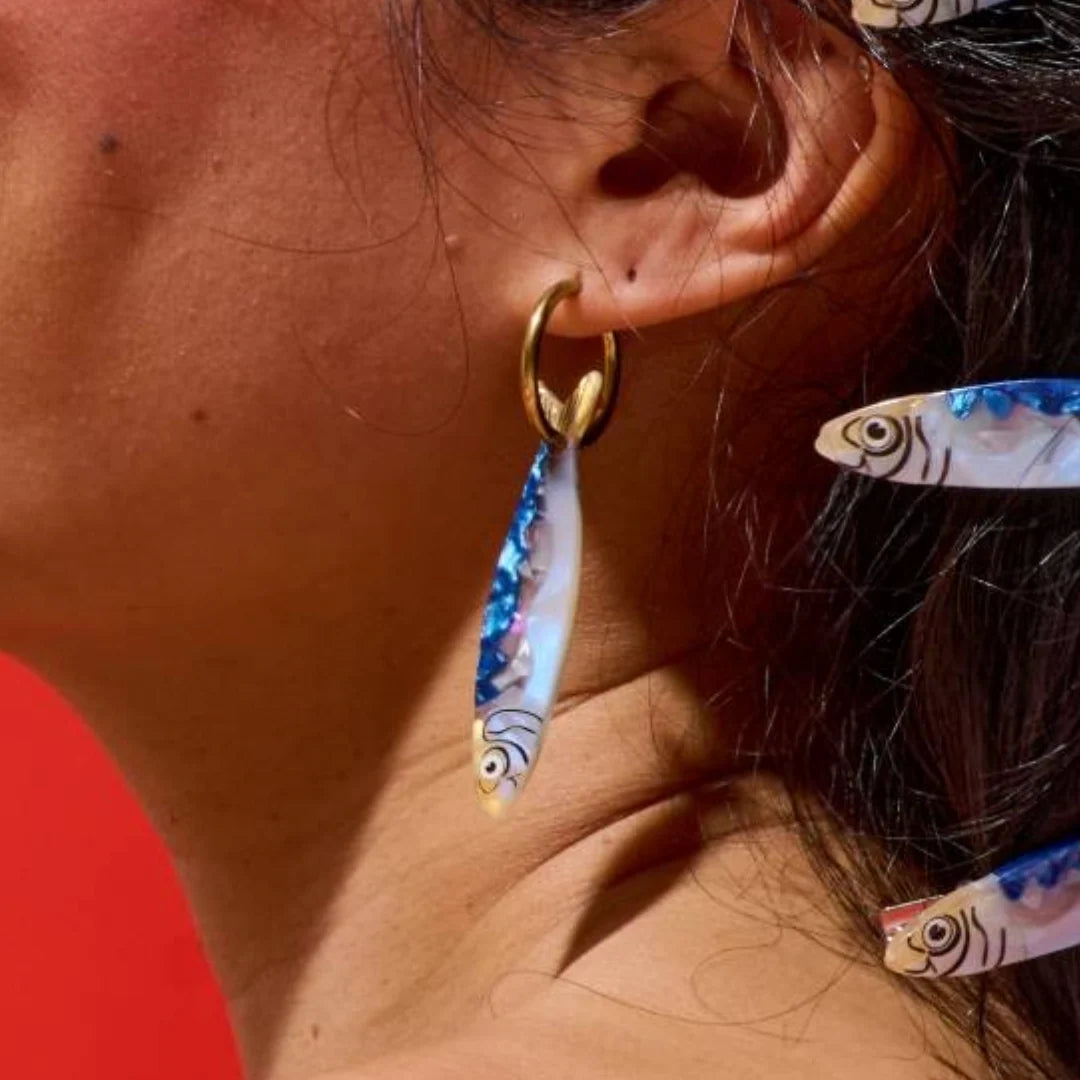 Close-up of a person wearing a gold hoop earring with a fish-shaped pendant.