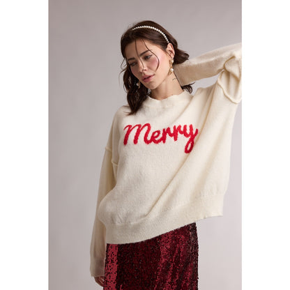 Woman wearing Cream sweater with the word "Merry" in red cursive on it with a red sequin skirt underneath on grey background