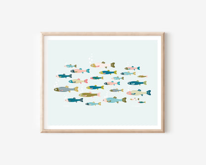 A framed art print featuring a colorful illustration of various stylized fish swimming in a light blue water scene, set in a natural wood frame against a white wall.