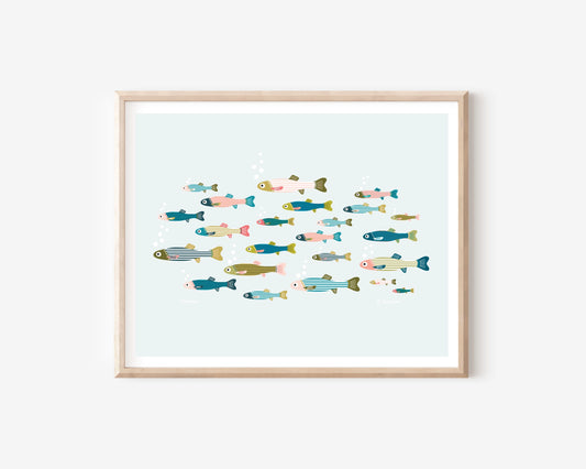 A framed art print featuring a colorful illustration of various stylized fish swimming in a light blue water scene, set in a natural wood frame against a white wall.