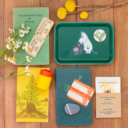 Green tray with Moomin Character with flowers and notebooks on a wooden table Birds eye view