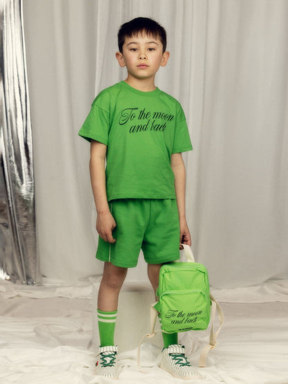 Child wearing a green outfit with text, holding a matching backpack against a neutral background