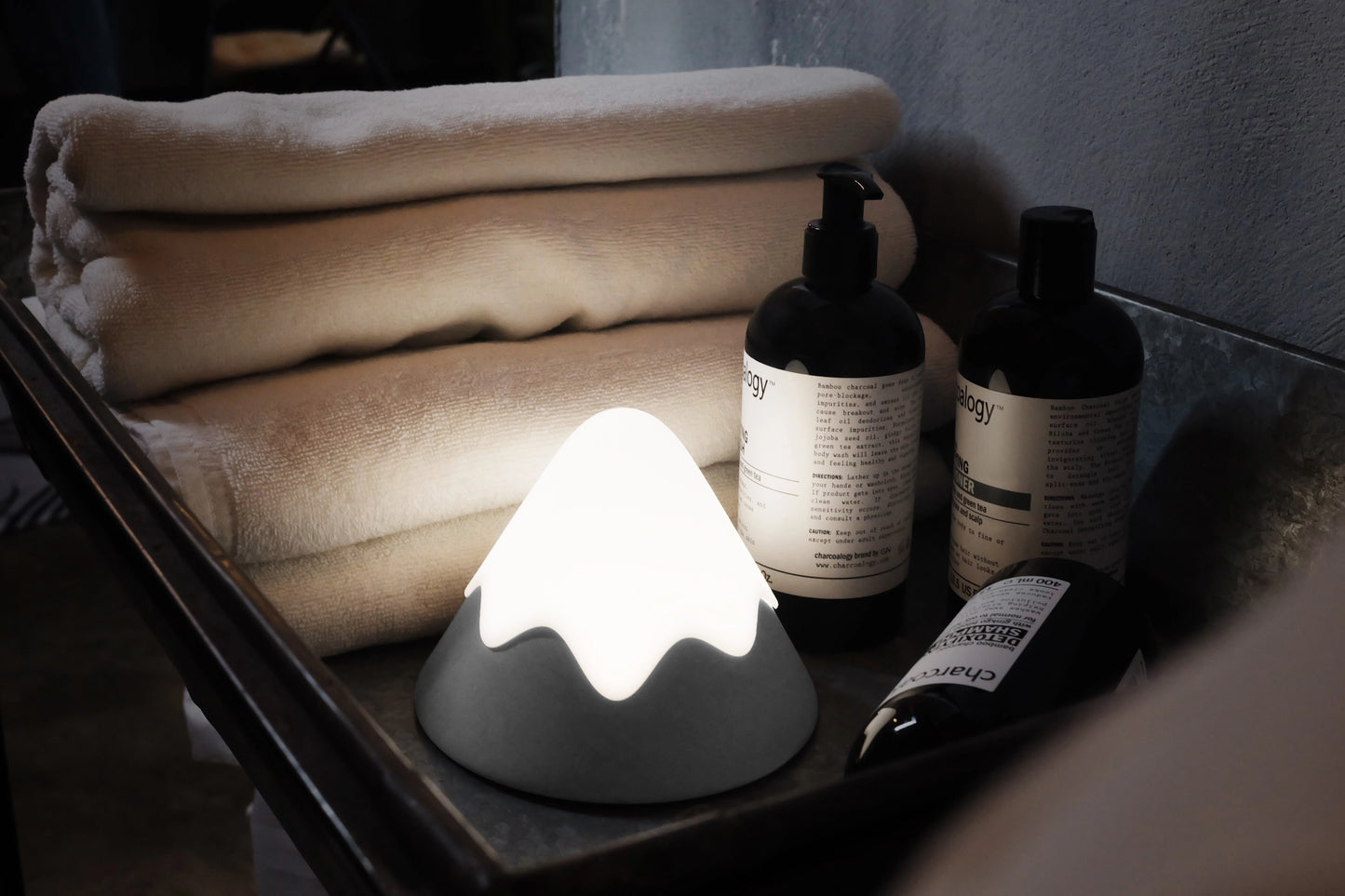 Bathroom tray with towels, bottles, and a mountain lamp emitting light.