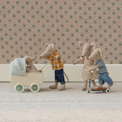 Maileg family of toy mice with a baby in a stroller, a son on a scooter, and a mother with a child on a scooter against a floral wallpaper background.