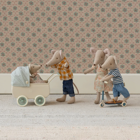Maileg family of toy mice with a baby in a stroller, a son on a scooter, and a mother with a child on a scooter against a floral wallpaper background.