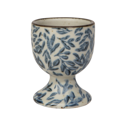 Ceramic egg cup with blue leaf pattern on a white background. Capture the essence of water, air, earth, and fire with the Myrtle Egg Holder from the Element collection. It soothes, revives, grounds and ignites— awakening our natural connection to the elements.