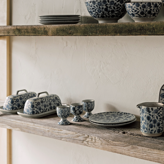 Ceramic tableware with blue floral patterns on wooden shelves against a neutral wall.