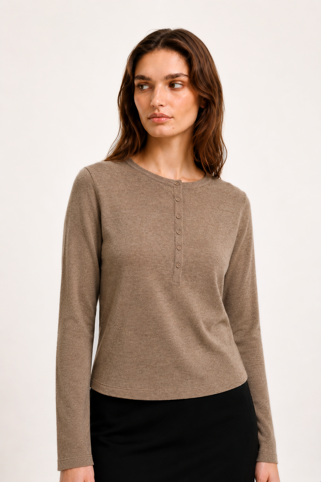 A woman modeling a taupe brown long-sleeve henley top with a button placket, paired with a black skirt, against a plain off-white studio background.
