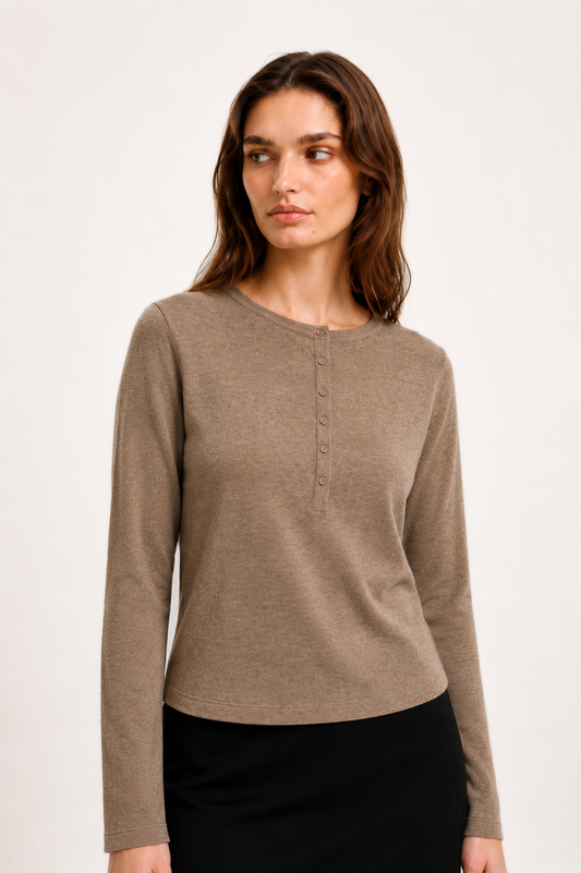 A woman modeling a taupe brown long-sleeve henley top with a button placket, paired with a black skirt, against a plain off-white studio background.