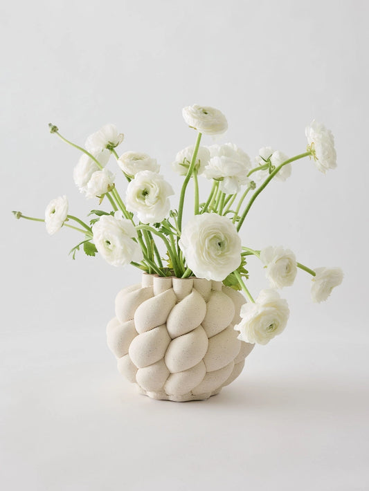 White vase with textured surface holding white flowers on a light gray background