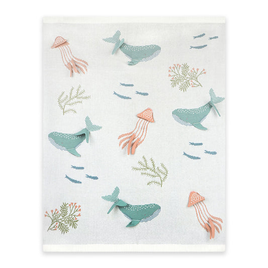 Baby blanket with ocean-themed illustrations of whales, squids, and seaweed on a white background