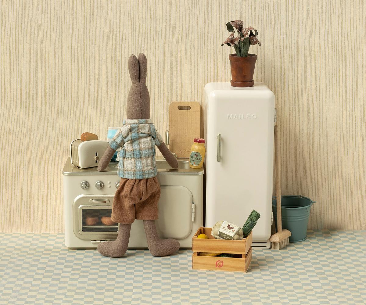 Stuffed animal rabbit in a kitchen setting with a refrigerator and oven.