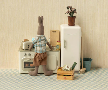 Stuffed animal rabbit in a kitchen setting with a refrigerator and oven.