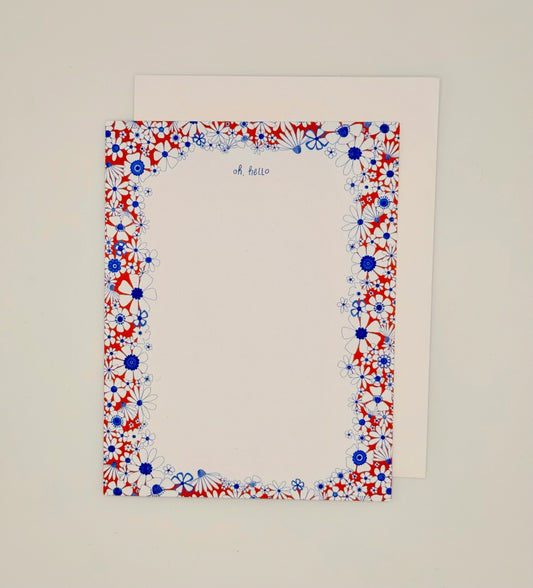 A square white stationery card with a red, white, and blue floral border and the words 'oh hello' printed at the top, shown with a white envelope behind it on a light neutral background.