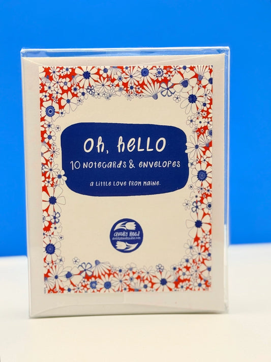 A boxed card set titled "Oh, hello: 10 notecards & envelopes" by Clover Leaf Studios, featuring a cream cover with a blue central label and a red, white, and blue floral border, photographed against a bright blue background.
