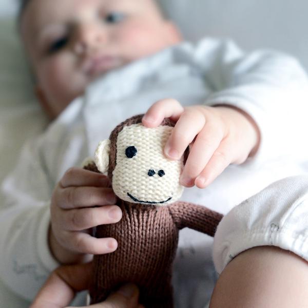 Baby holding a knitted monkey toy with a blurred background