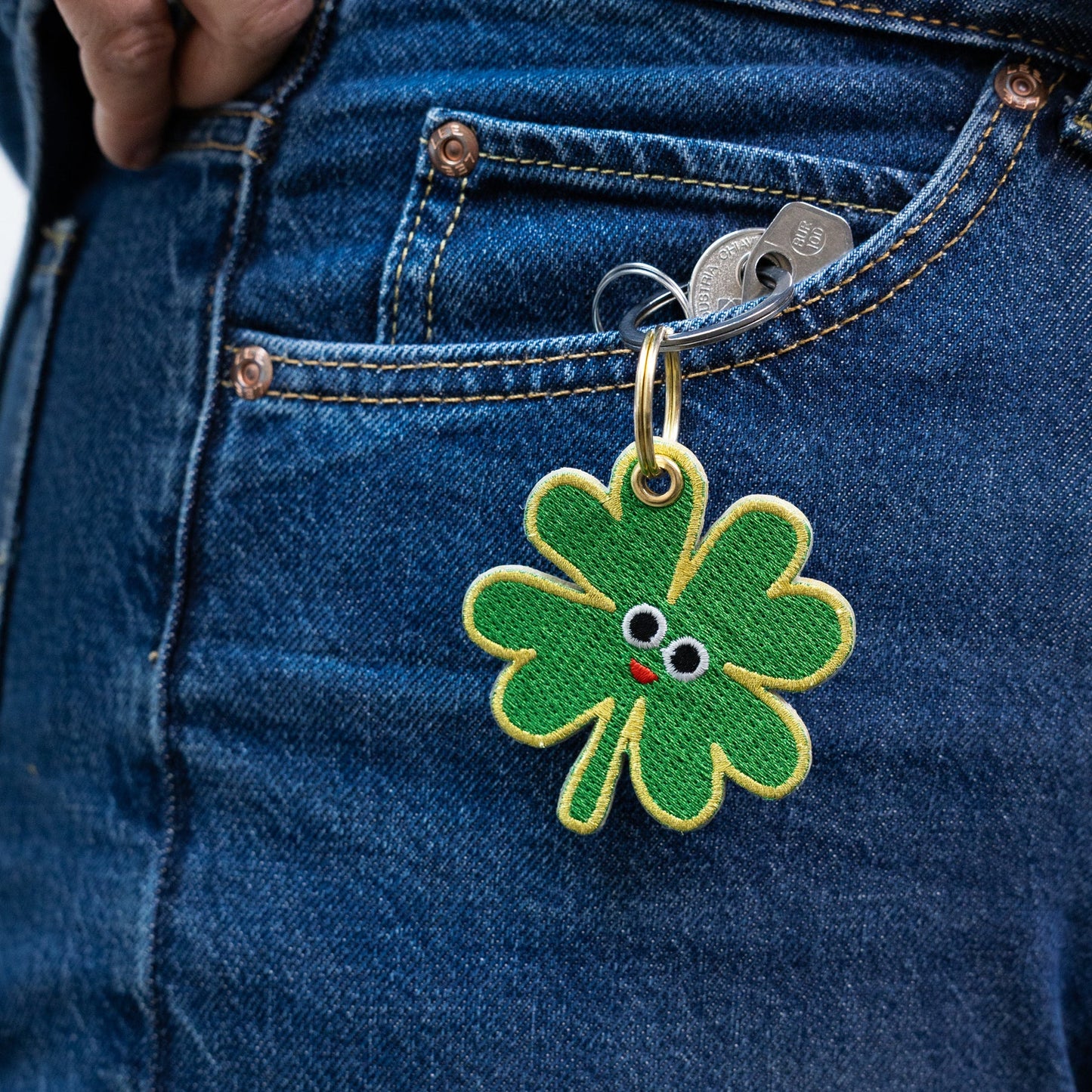Green four-leaf clover keychain with a face attached to blue denim jeans.