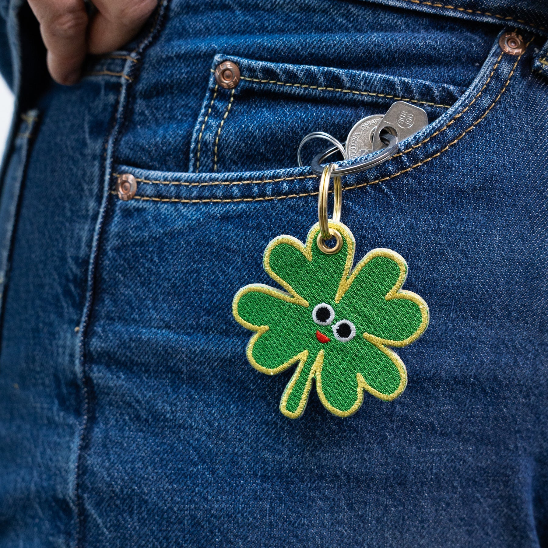 Green four-leaf clover keychain with a face attached to blue denim jeans.