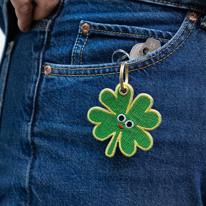 Green four-leaf clover keychain with a face attached to blue denim jeans.
