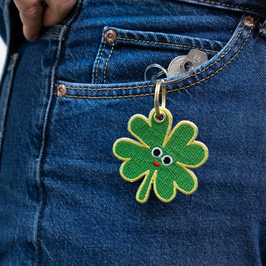 Green four-leaf clover keychain with a face attached to blue denim jeans.