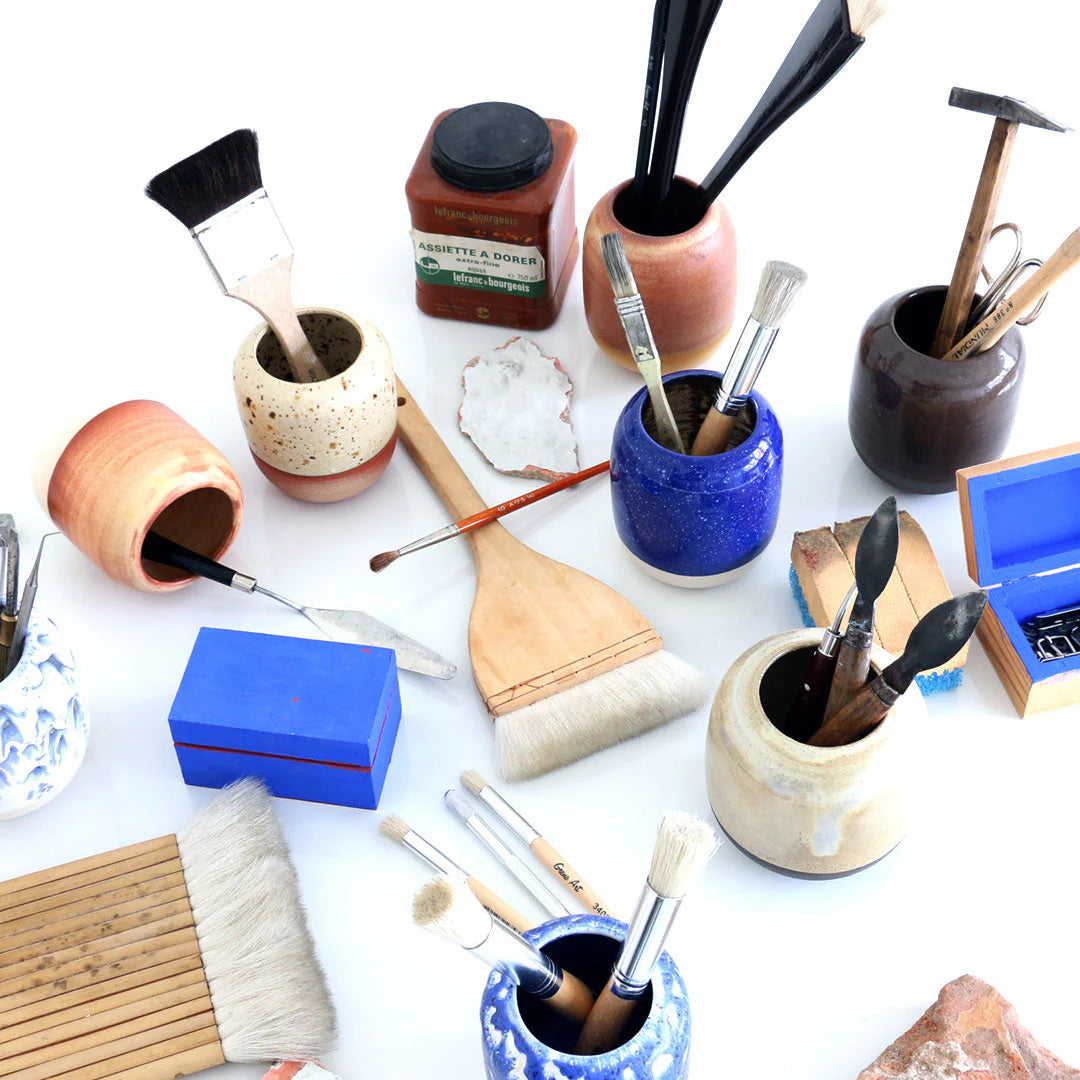 Collection of painting tools including brushes, jars, and a palette on a white surface.