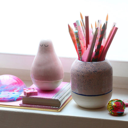 Pink ceramic lamp and speckled ceramic jar with pencils on a windowsill