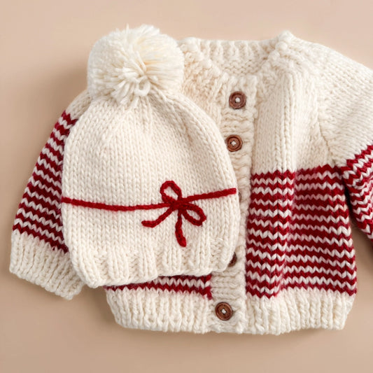 A fun Holiday hat to celebration the biggest gifts in life. Features a yarn Red bow and Cream yarn pom. Pair this hat with the matching sweater or a coordinating cardigan.