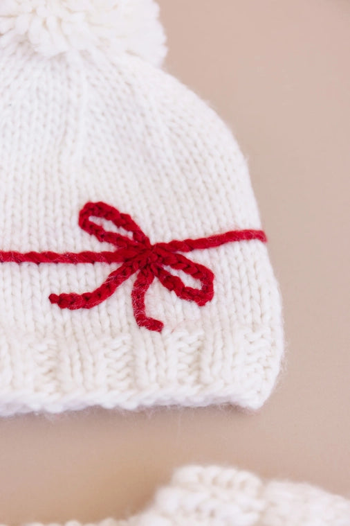 A fun Holiday hat to celebration the biggest gifts in life. Features a yarn Red bow and Cream yarn pom. Pair this hat with the matching sweater or a coordinating cardigan.