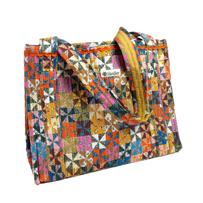 A quilted tote bag featuring a vibrant, multicolor geometric patchwork pattern with a mustard yellow zipper and handles, shown on a plain white background.