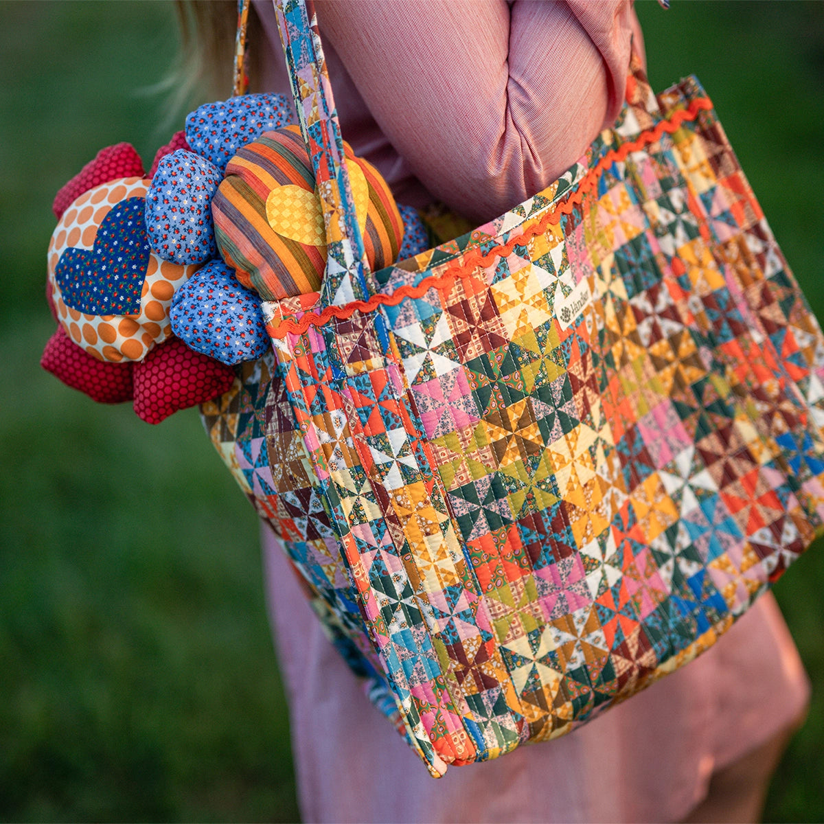 Colorful Quilted Tote held by woman wearing pink dress on green grass background