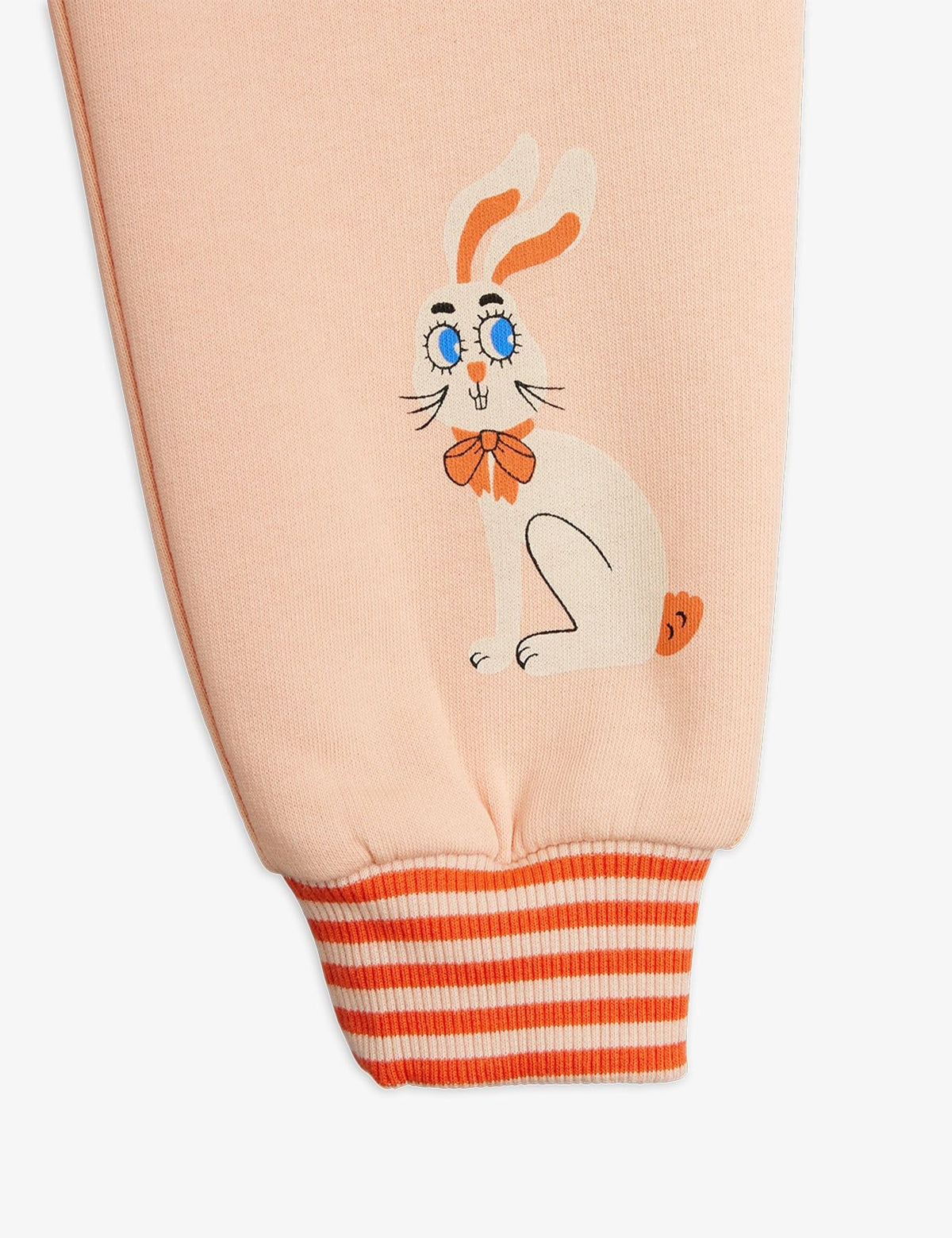 Close-up of a light peach sweatshirt sleeve featuring a cartoon rabbit graphic with blue eyes and an orange bow tie, finished with an orange and white striped ribbed cuff.