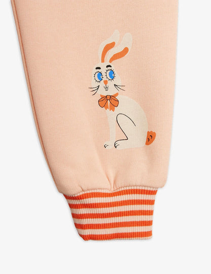 Close-up of a light peach sweatshirt sleeve featuring a cartoon rabbit graphic with blue eyes and an orange bow tie, finished with an orange and white striped ribbed cuff.