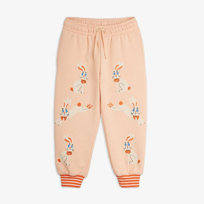 Light peach pink sweatpants featuring a playful cartoon bunny pattern, elastic waistband with drawstring, and orange-and-white striped cuffed ankles, shown flat on a light gray background.
