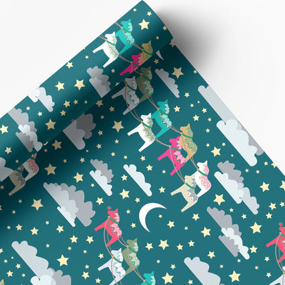 A roll of wrapping paper or fabric with a whimsical night-sky pattern, featuring colorful reindeer, stars, clouds, and a crescent moon on a teal background.