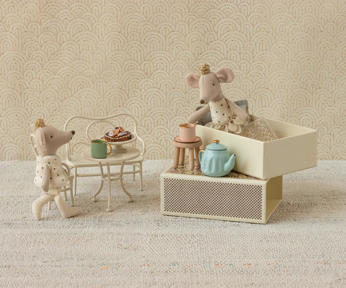 Miniature mouse figures with a tea set on a textured surface with a patterned wall background.