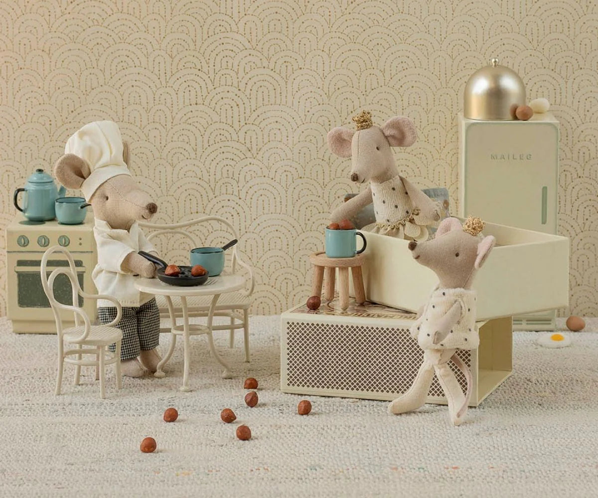 Three toy mice in a kitchen setting with a patterned wallpaper background.