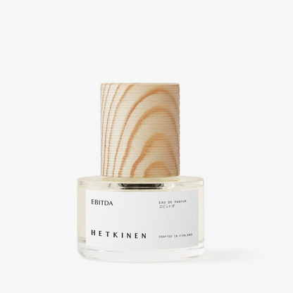 A clear glass bottle of EBITDA Hetkinen Eau de Parfum with a white label and a light natural wood grain cap, set against a plain white background.