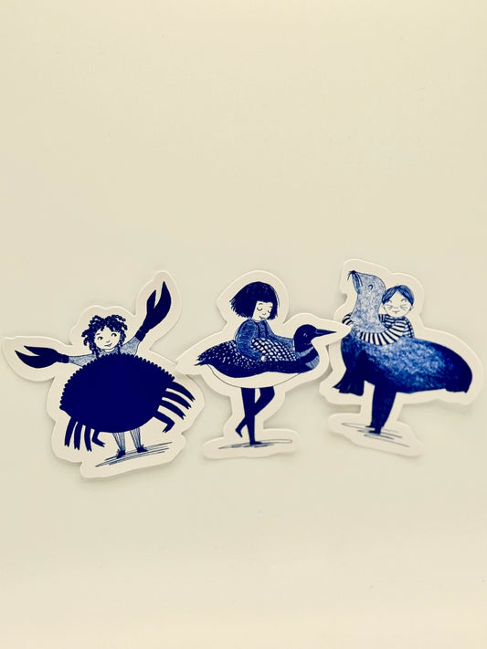 Three die-cut stickers featuring whimsical blue and white illustrations of a crab, a loon, and a duck, displayed on a light cream background.