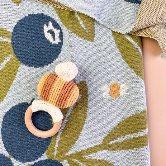 A whimsical baby blanket, adorned with juicy blueberries, busy bees, and Harper Bear. Crafted with utmost care, this blanket is made from 100% GOTS certified organic cotton, ensuring the softest and safest embrace for your baby's delicate skin. Paired with our adorable bee rattle teether made from soft cotton and beech wood for safe chewing, and a cotton baby hat with ears. Makes a great baby or newborn shower gift! Find it at Huset Shop in Venice California