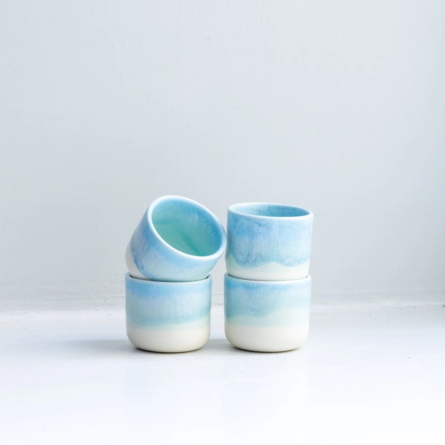 Set of four ceramic cups with blue and white gradient on a light gray background