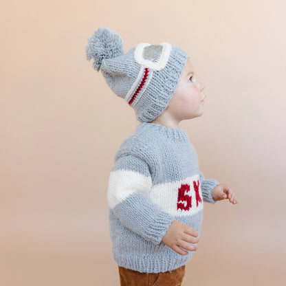 Child wearing a knitted sweater and hat with a neutral background