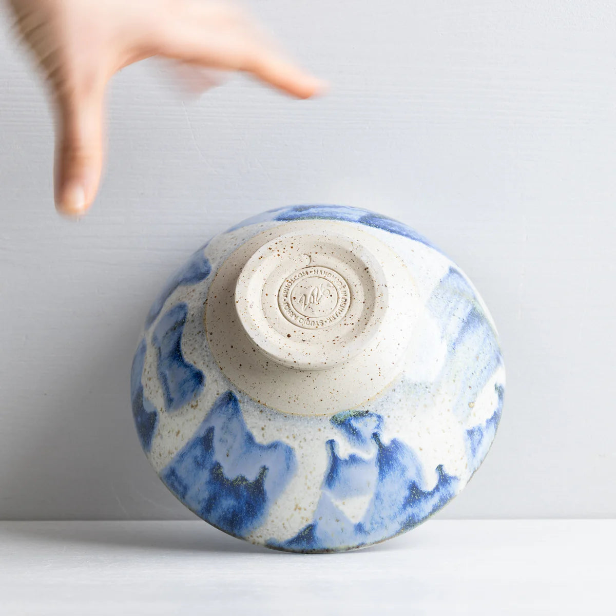 Blue Ceramic Bowl upside down With a hand on a white background