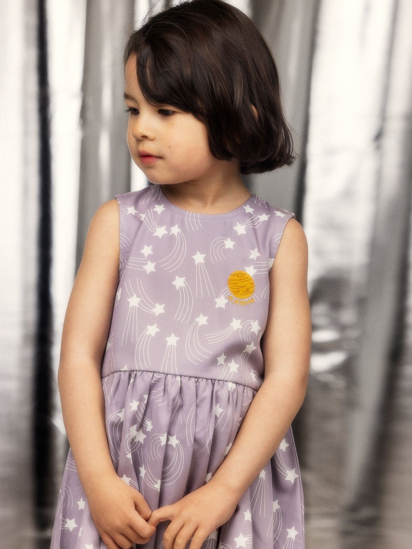 Sleeveless dress made from 100% lyocell. Features the Starfall print, a gathered skirt with bubble hem, and a small embroidered planet patch. Back neck keyhole with snap closure.