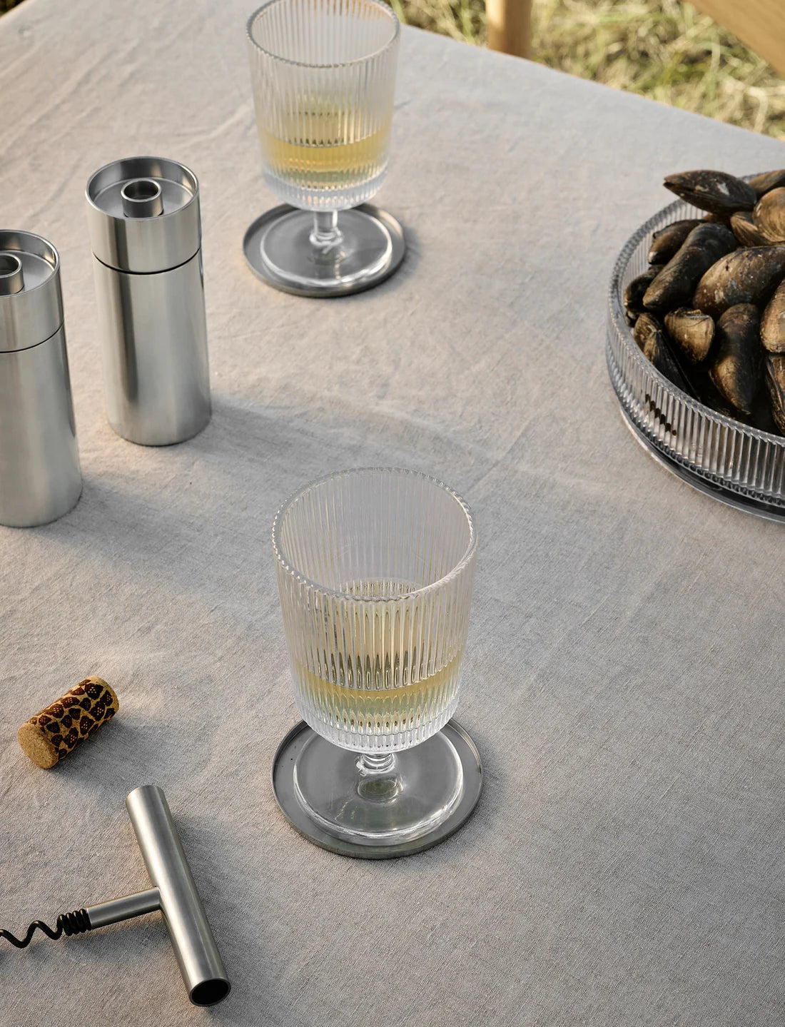 Clear glass with a drink on a textured surface with a corkscrew and small bowl of snacks.